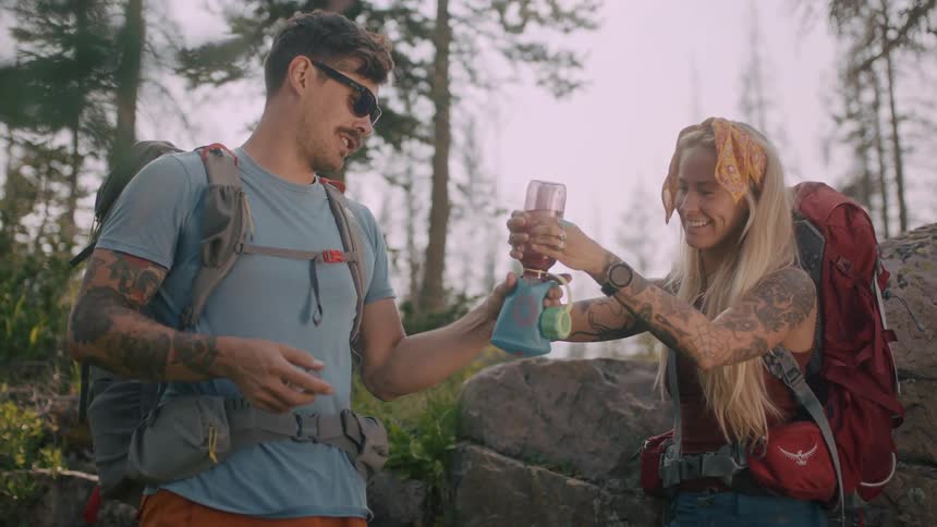 A woman laughs as she squeezes liquid through a filter while out hiking with a man