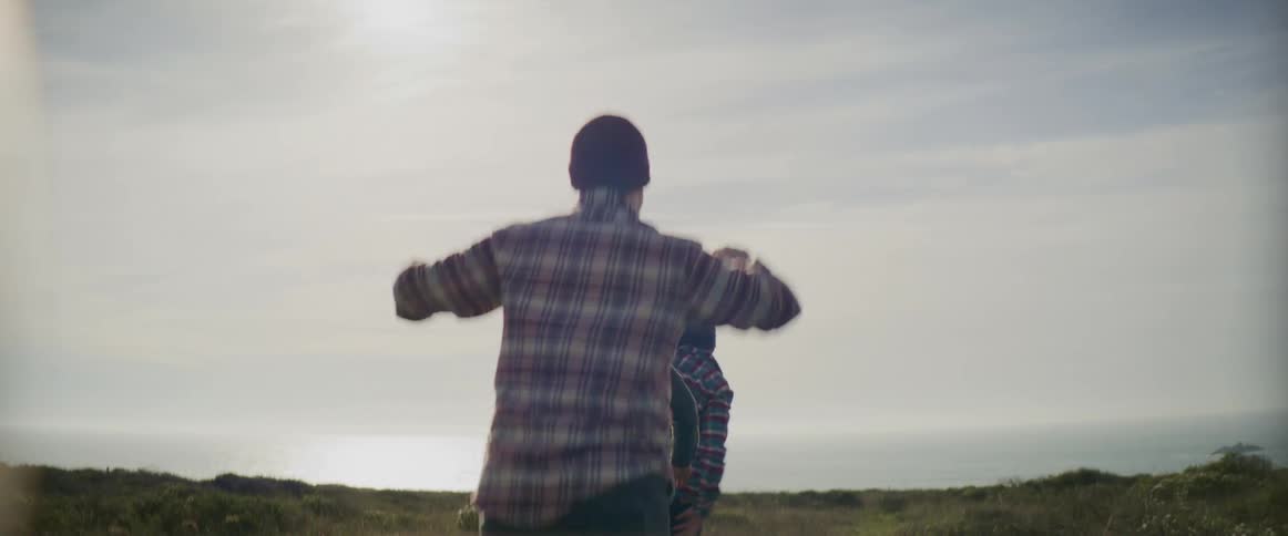 Three men jump an throw their arms in the air as they run across a grassland