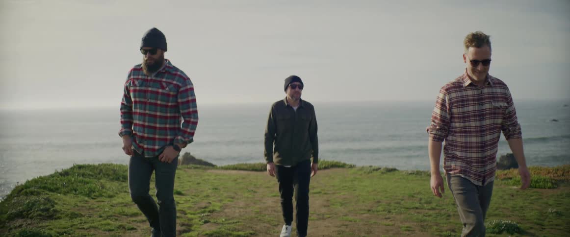 Group of friends walking over grass near the ocean at sunset