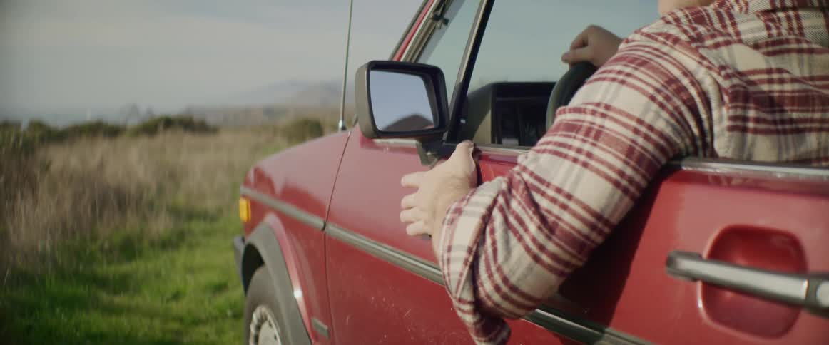 Man sitting on a red car waiting while parked on a clearing in the countryside