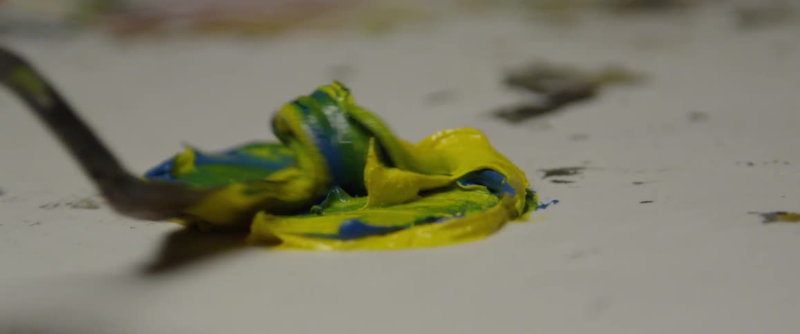 Someone mixes blue and yellow paint