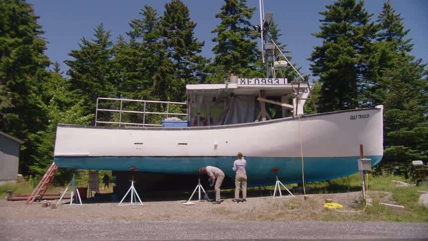 A man and woman paint the hull of a grounded boat on a clear day