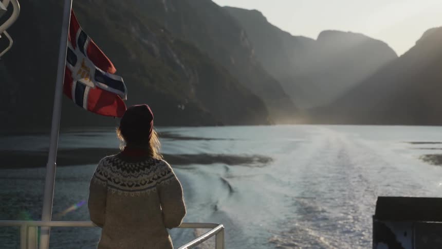 A woman is riding on a boat next to a flag at dusk
