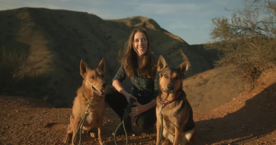 A woman is sitting outdoors next to her two dogs