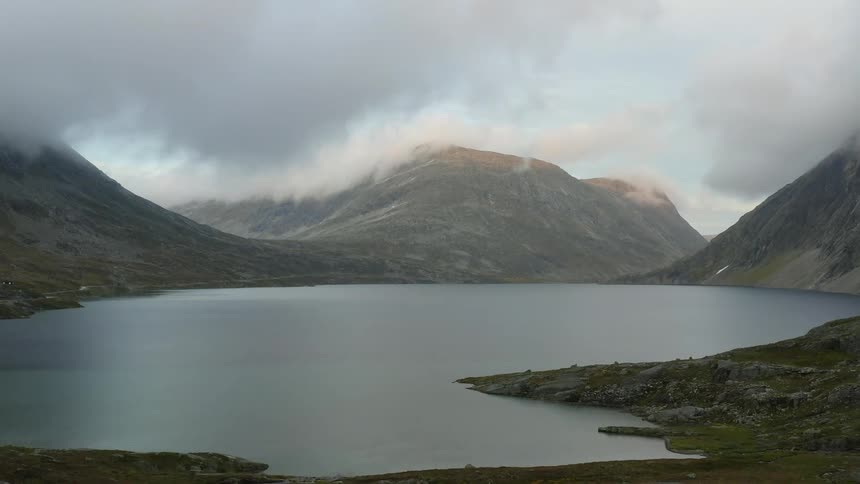 Thick clouds float over a lake surrounded by mountains