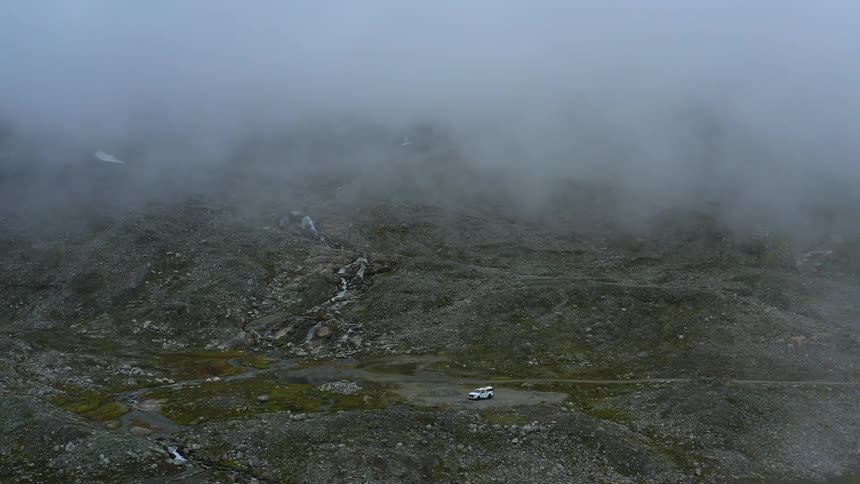 Aerial view of a white car parked on a clearing near the mountains under the clouds