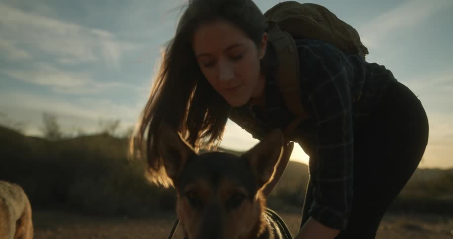 A woman leans down and kisses her german shepherd on the head while on a hike in a flat weedy area