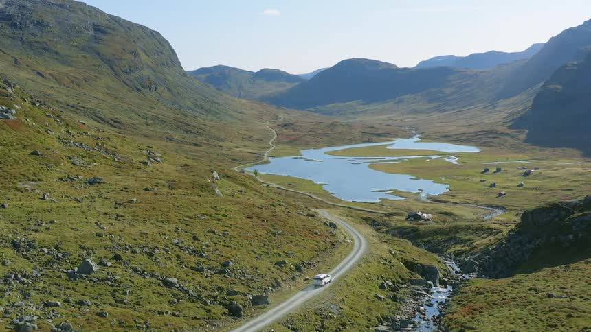 A vehicle travels along a road through a mountain valley on a sunny day
