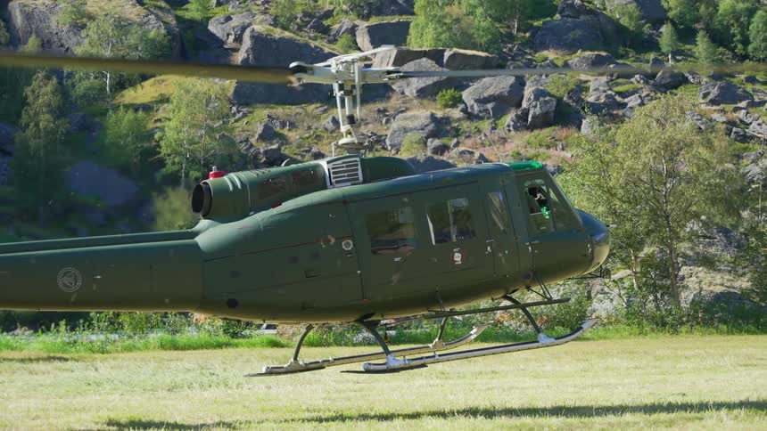 A green helicopter is sitting on the grass with the rotor turning and lifts off the ground