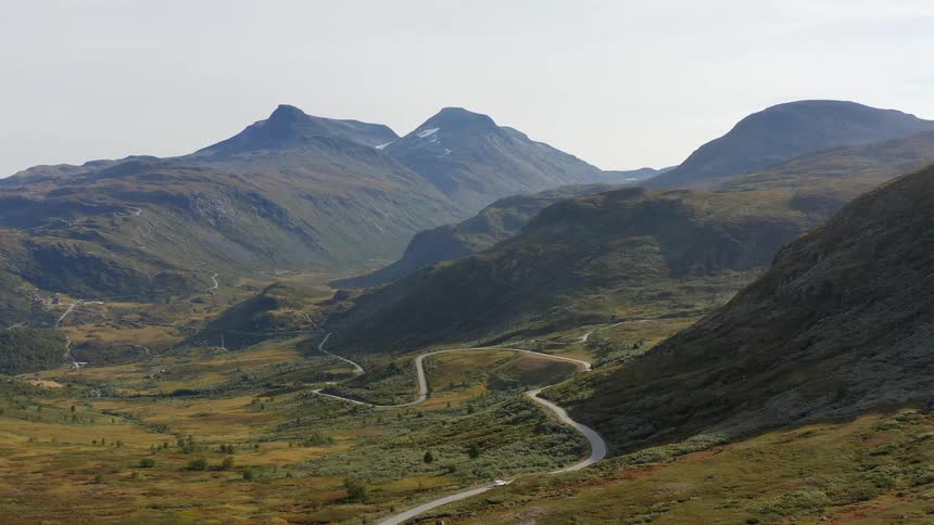 A car travels on a winding road through grass covered mountains