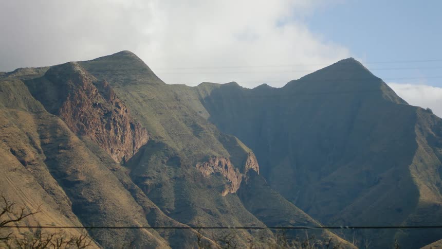 Grass covered mountains with peaks high in a cloudy sky