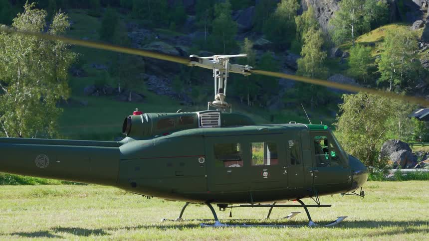 A green helicopter is sitting on the grass with the rotor turning