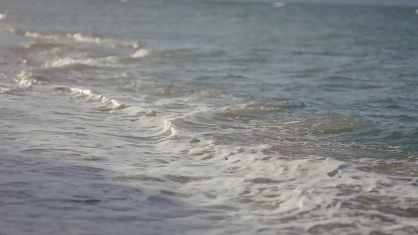 Small frothy waves roll onto a sandy beach