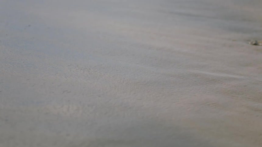 The tide washes in and out of a sandy beach during the day