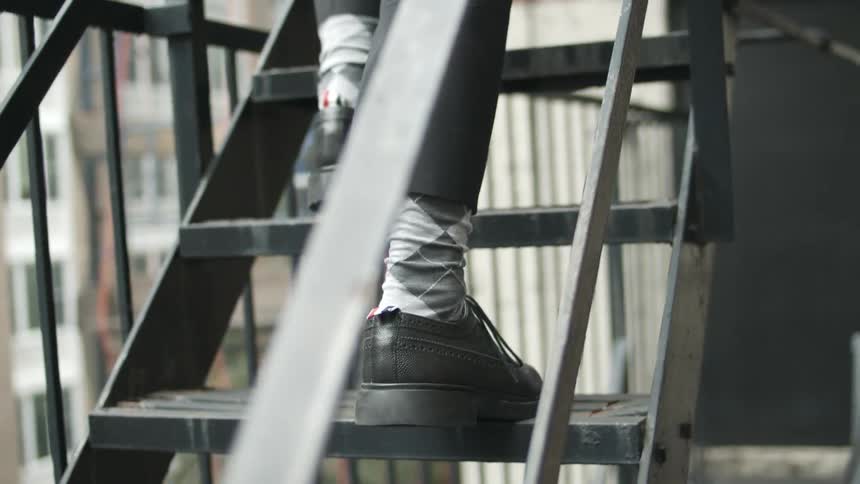 Close up of a man wearing black shoes with gray socks climbing stairs outside a building in the city