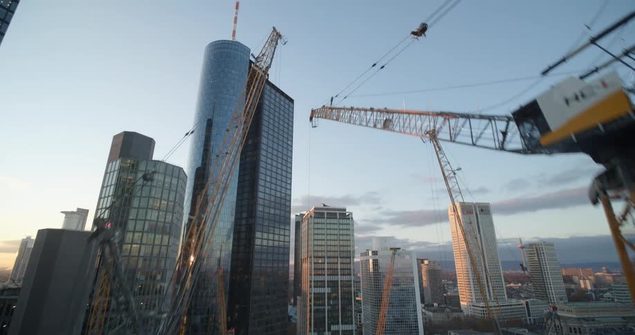 Aerial view of yellow construction cranes surrounded by skyscrapers in the city downtown at sunset