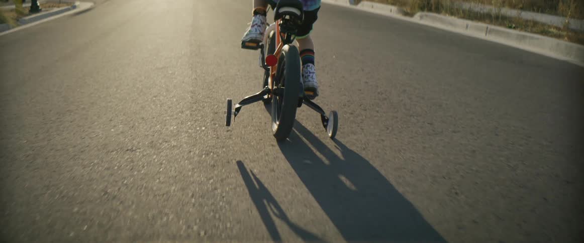 Little boy riding a bicycle with training wheels on the road at sunset