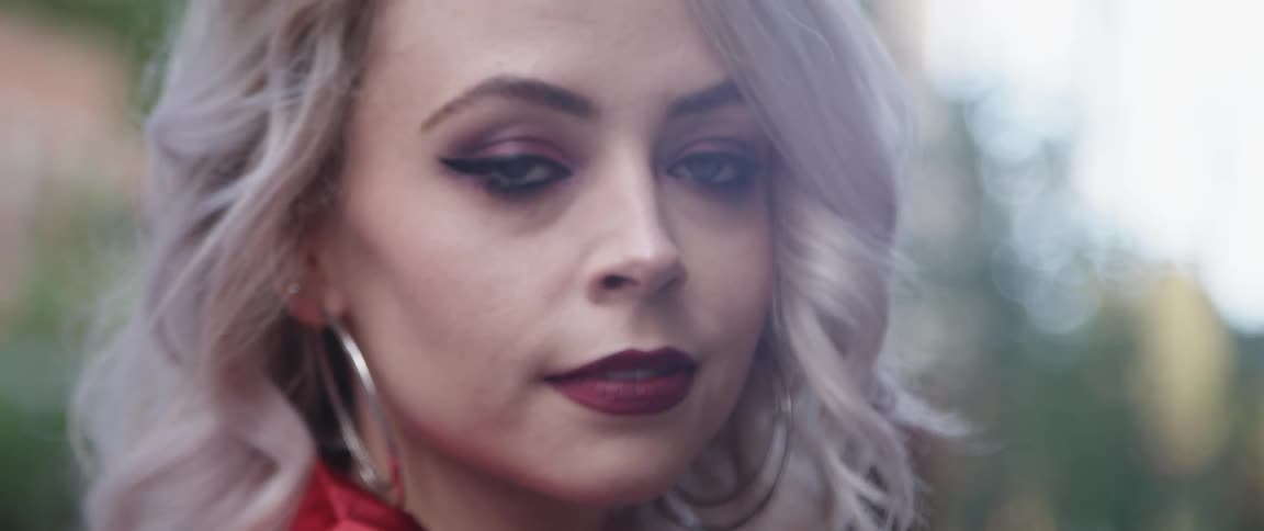 A young blonde haired woman wearing gold hoop earrings is looking forward and then looks away
