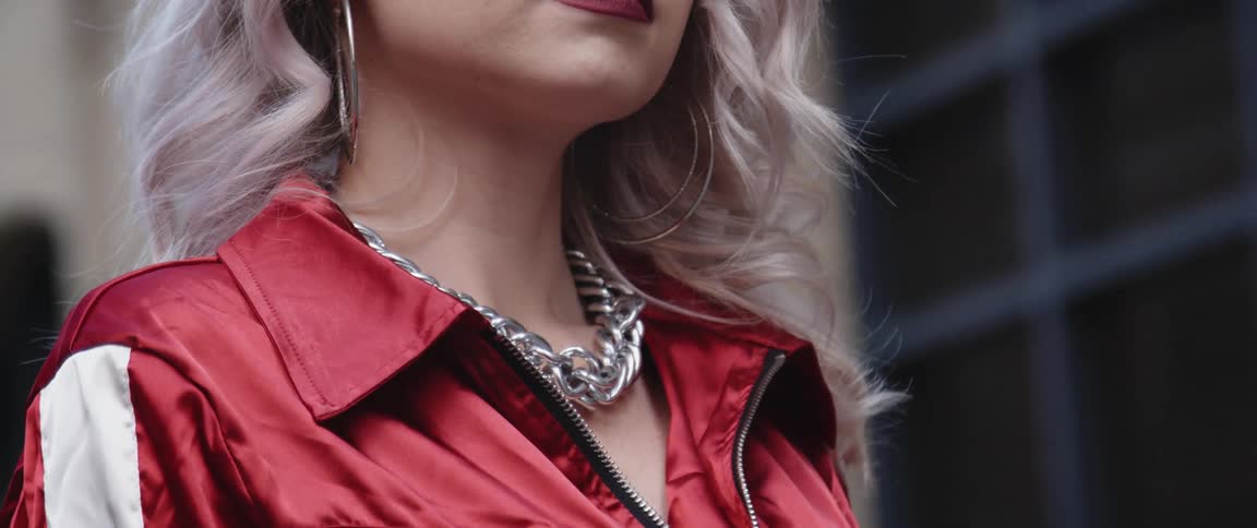 Young woman with bleached curly hair wearing a bright red jacket and a silver necklace