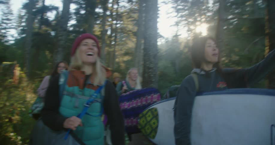 Group of friends carrying surfboards walking on a forest at morning