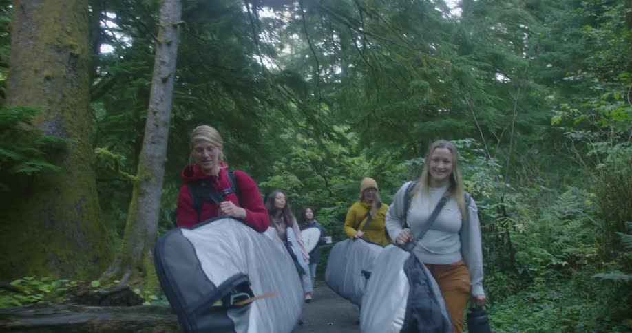Group of women carrying surfboards walking on a trail through the forest