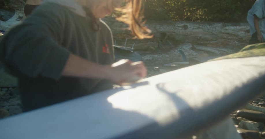 Women are waxing their surfboards on the beach