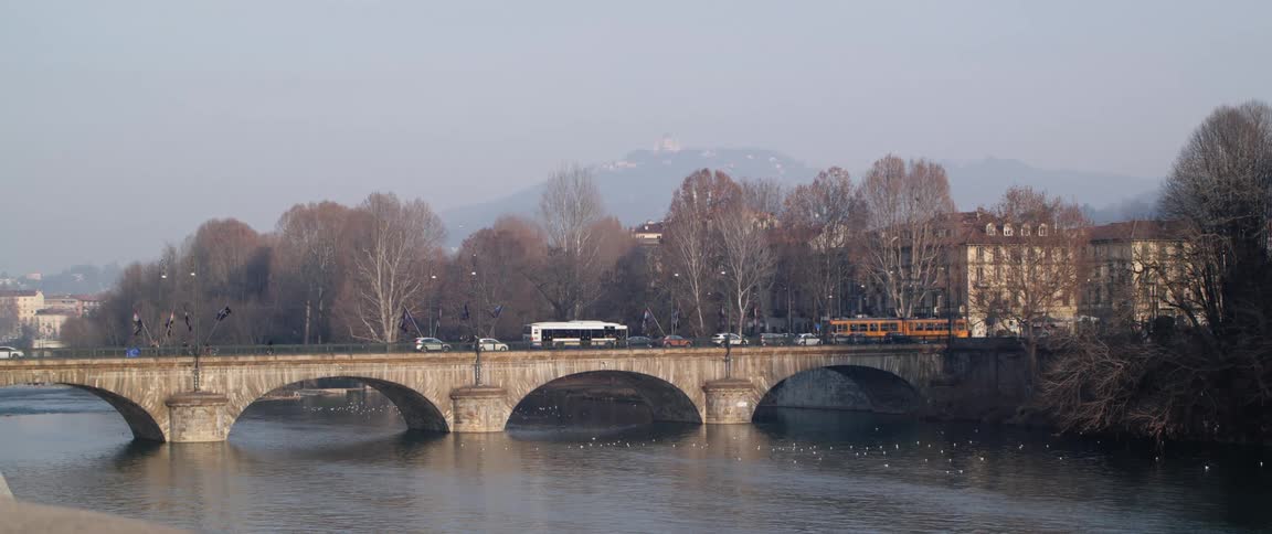 Vehicles driving over an arched bridge over a river through the city in the morning