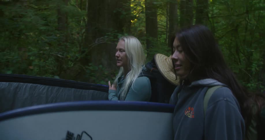 A group of surfers carrying surfboards walks in the woods