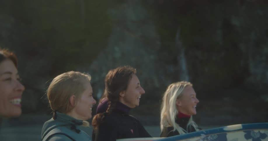 A group of women are walking on the beach with their surfboards