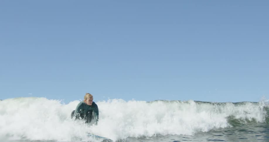 A female surfer lying on her surfboard starts to stand on her board as she rides a wave
