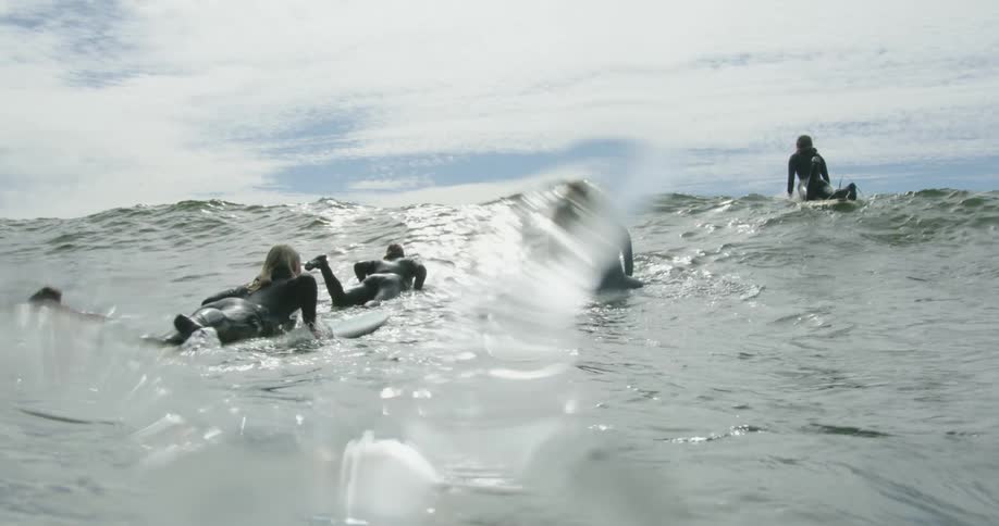 A group of women lie together on their surfboards as they float over an incoming wave