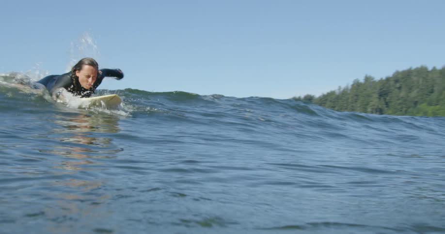 A woman lays on a surfboard and paddles through a wave