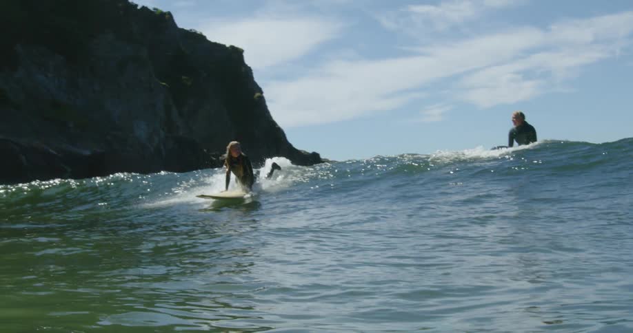 Surfers ride wave with promontory in the background