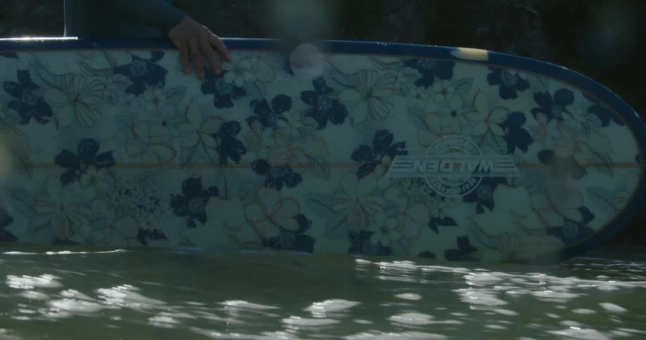 Woman carrying a surfboard with flower prints enters the ocean walking