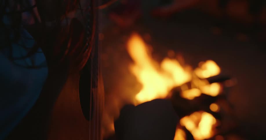 Woman plays ukulele next to bonfire at night on the beach