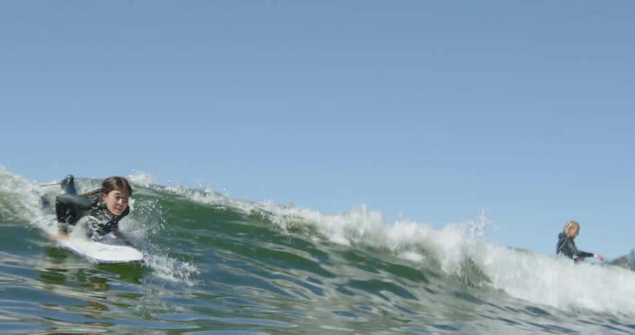 Two women paddle their surfboard to ride a wave