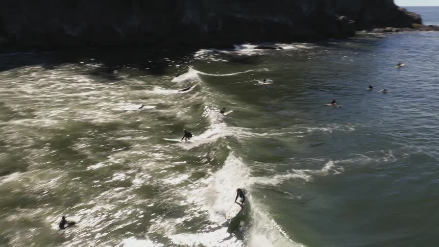 Group of women riding surfboards over the ocean waves close to the beach near a mountain