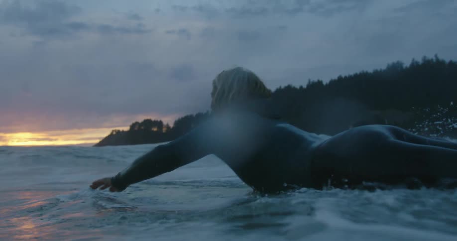 Two women swimming over surfboards on the ocean waves near the mountain at morning