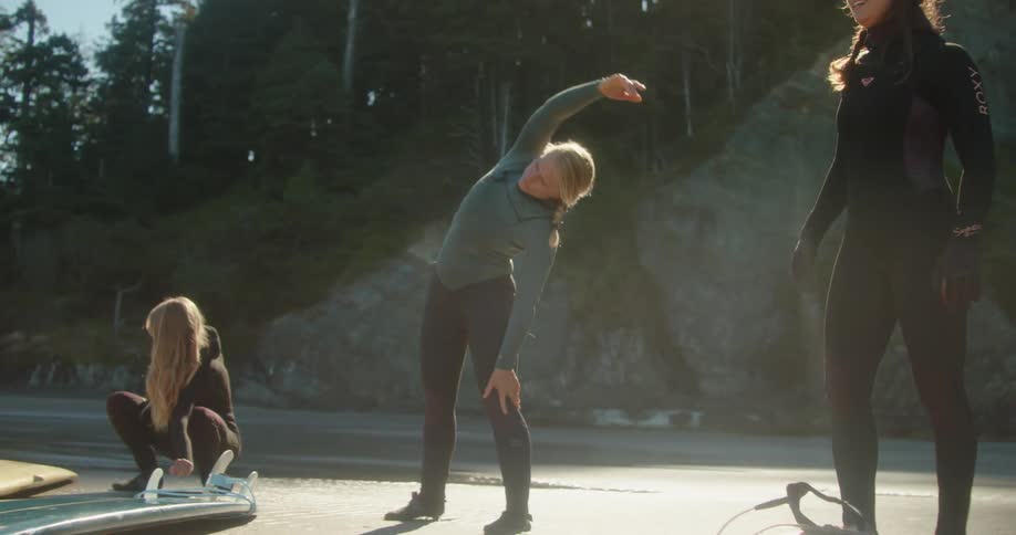 Women stretch on the beach near their surfboards