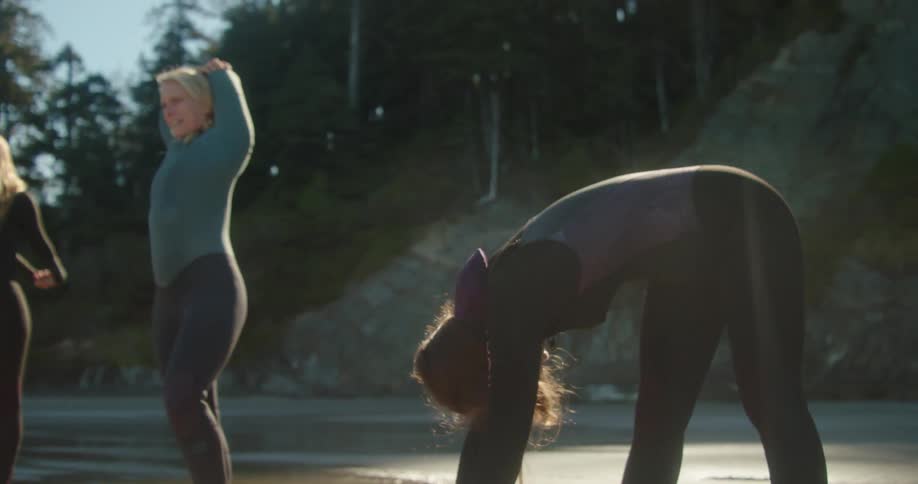 Women in wet suits stretch by the shore