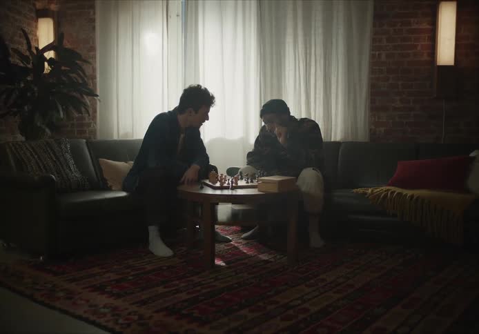 Two men are inside sitting down playing a game of chess