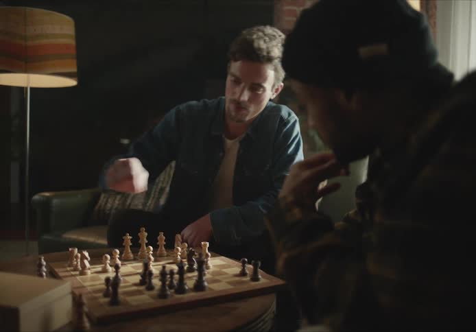 Two men play chess by the window