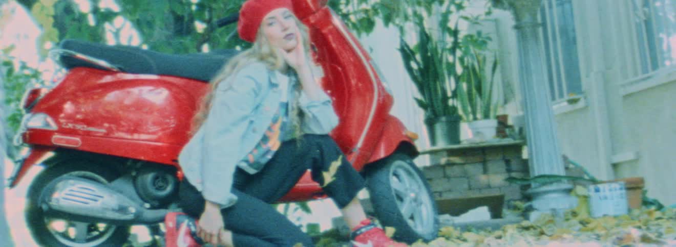 A woman posing kneeling in front of a red moped