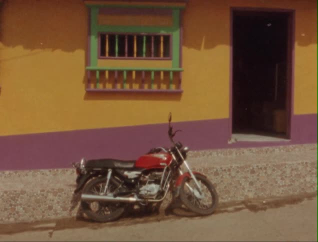 Motorcycle parked outside the colorful facade of a house caught on vintage film