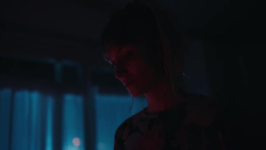 A woman stands in a dark room in her home and looks down
