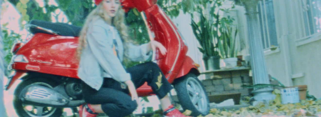 A teenage girl is posing next to a red moped