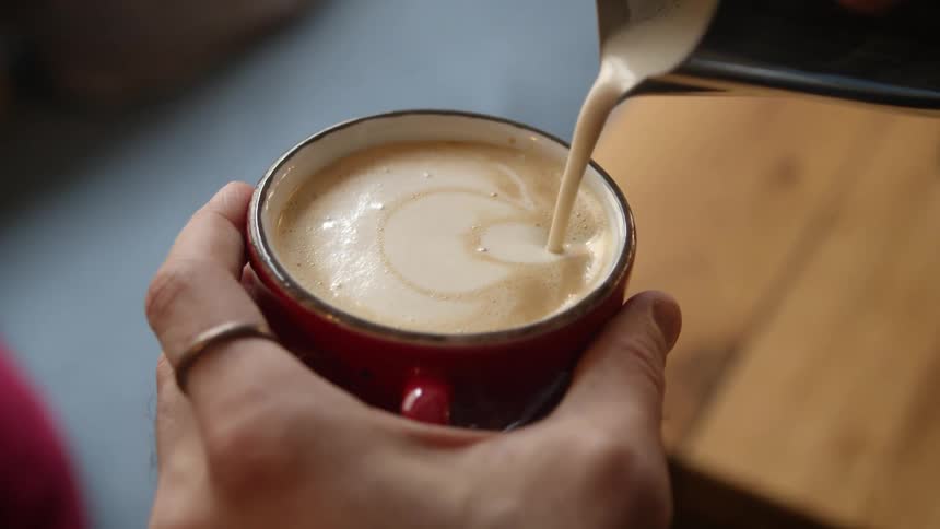 A person is pouring cream on the latte