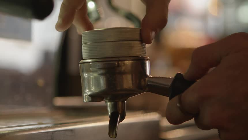 Barista screwing the top of an espresso filter to prepare coffee in the shop