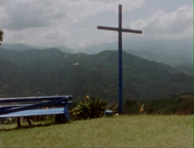 A blue bench beside a large cross overlooking mountains