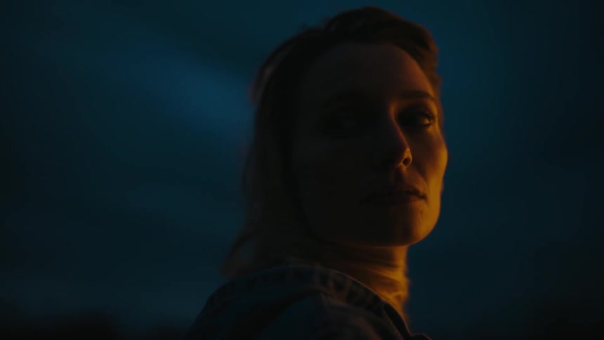 Woman with brown hair and black sweater looks over her shoulder at night